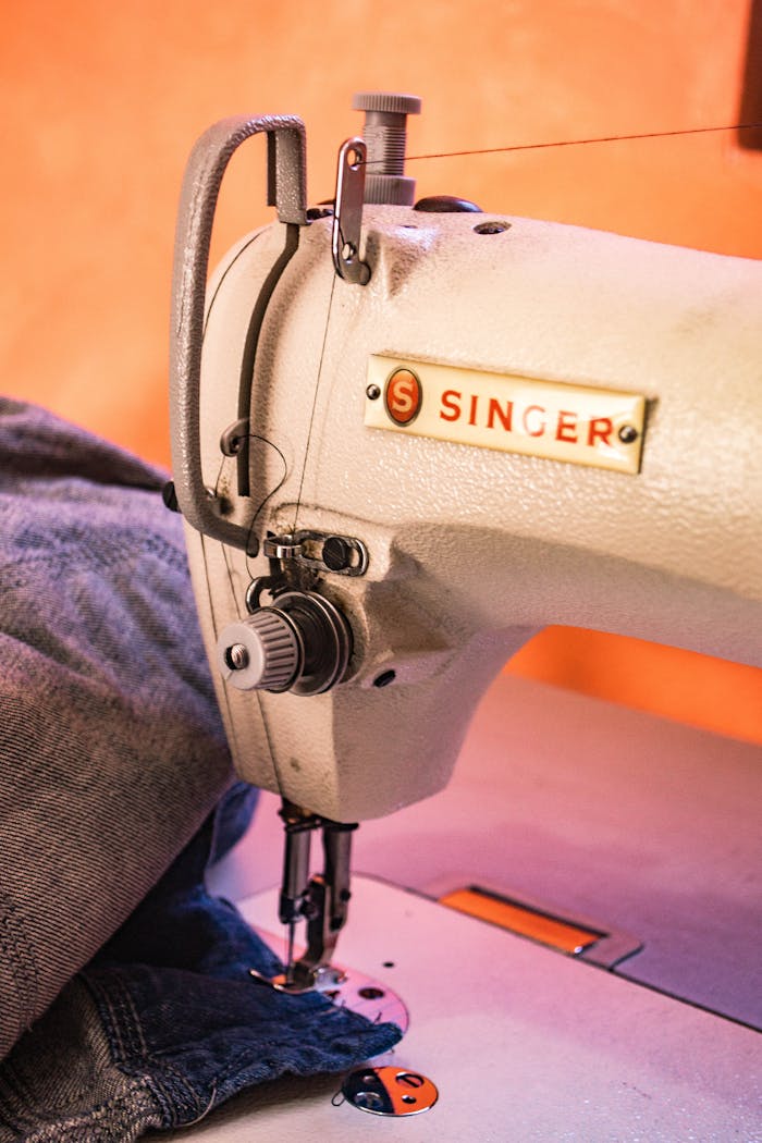 our-services-1 Detailed view of a Singer sewing machine working on denim fabric with precision.